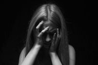 Black and white photo of an obscured woman with her head in her hands in pain.