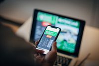 Man using mobile app for live betting and online gambling and watching a sports match