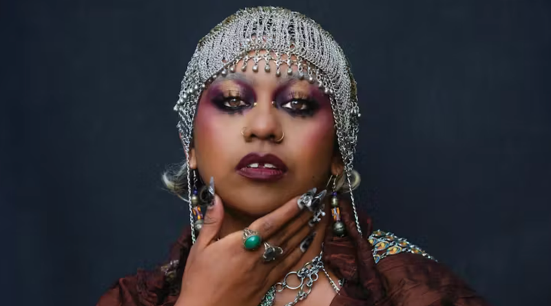 Portrat headshot of Emily Wurramara in a netallic headdress holding to hand to her chin