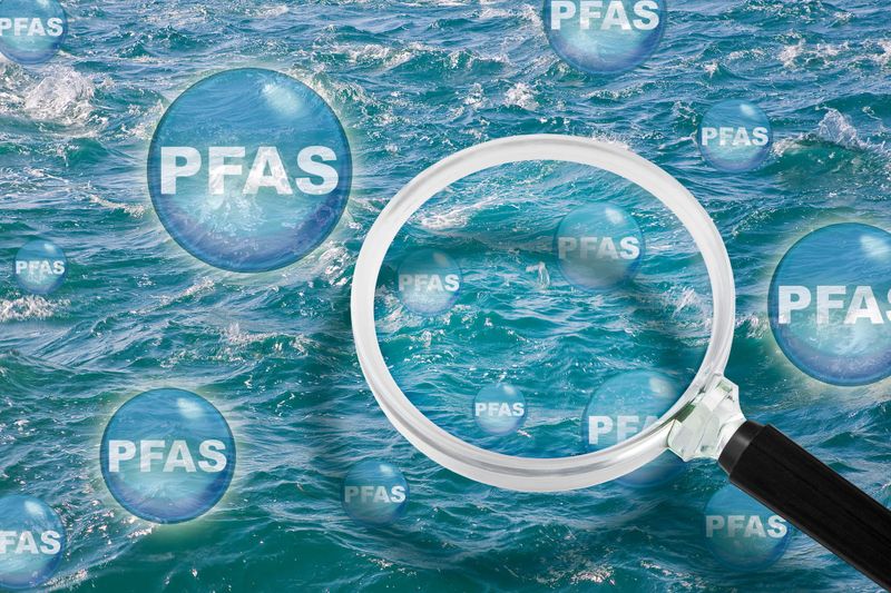 Concept image with water background, and a magnifying glass surrounded by circles with text reading 'PFAS'