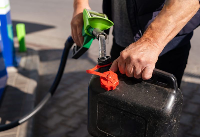 A man filling a jerry can at a petrol station bowser