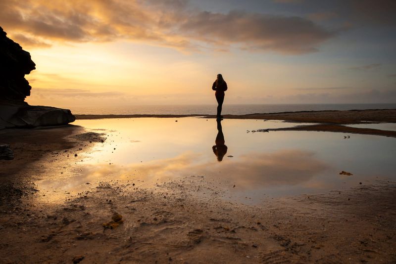 Woman and her reflection in water, watching the sunrise