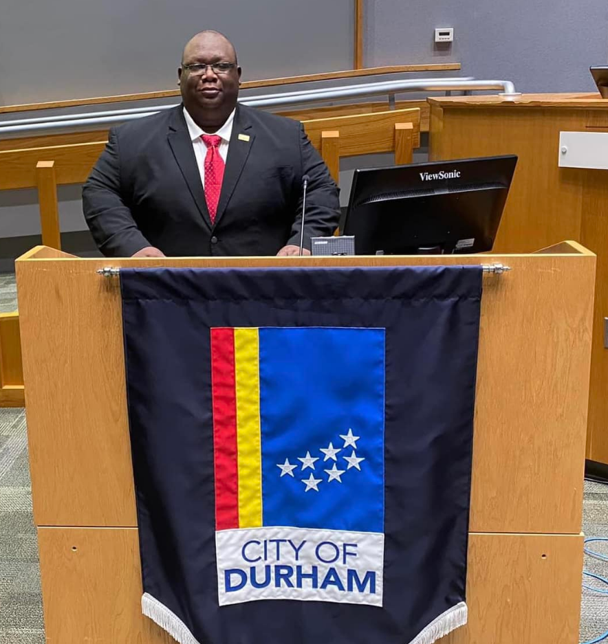 DeWarren K. Langley stands at the podium in Durham City Hall behind the City of Durham banner. Langley, a respected advocate for youth empowerment and community development, was remembered by city leaders following his passing.