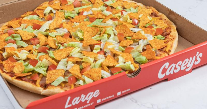 An image of a large pizza in a box labeled Casey's. It is a thin crust pizza with lettuce and tomato and some kind of tortilla like chip on top.