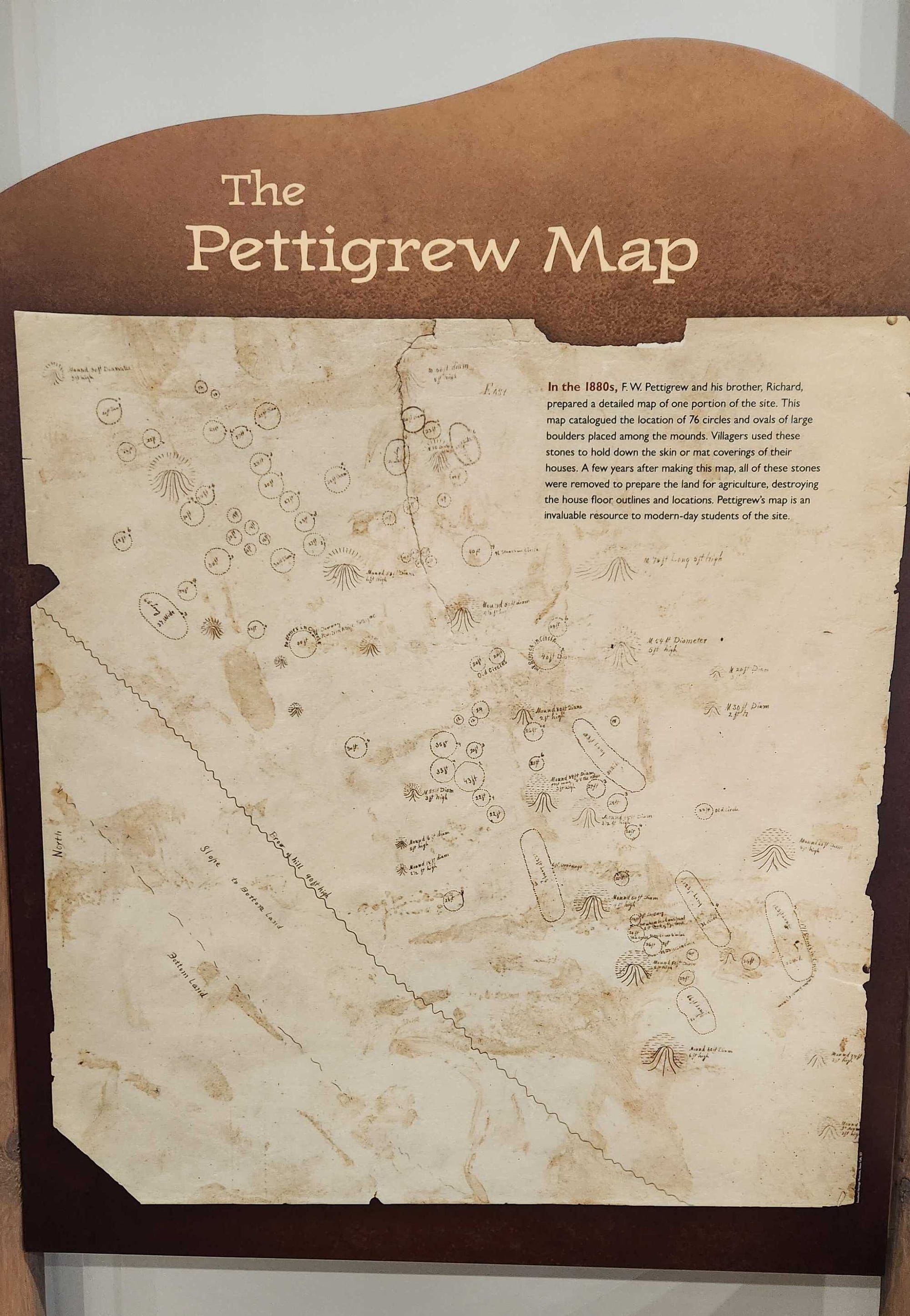 A museum display panel titled "The Pettigrew Map" showing an aged, hand-drawn 1880s map cataloguing 76 circles and ovals marking large boulder placements among mounds at a Native American village site, accompanied by explanatory text noting the stones were later removed for agriculture, making this map an invaluable historical record.