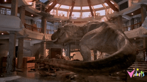 A Tyrannosaurus rex rampages through the destroyed visitor center lobby in a scene from Jurassic Park, illustrating the author's analogy about AI "filling in gaps" with hallucinated information the way frog DNA was used to fill gaps in dinosaur DNA—with similarly chaotic results.