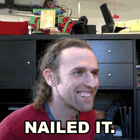 A smiling man with long hair and a red sweater, captioned "NAILED IT." — expressing satisfaction after successfully completing the desk robot build described in the article.