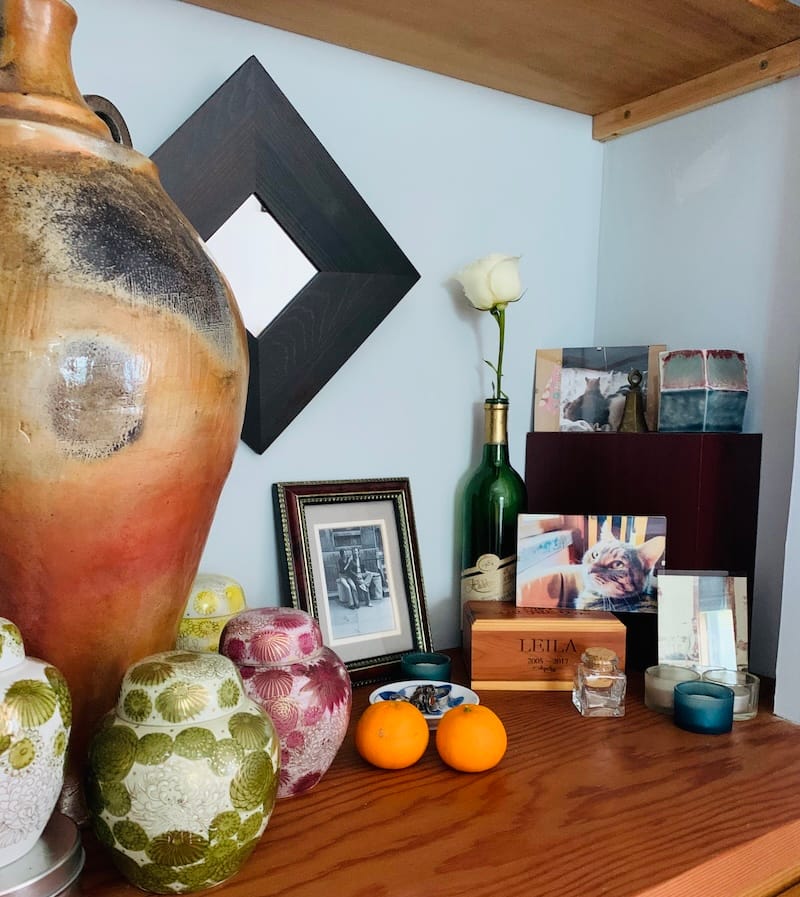 My altar, which includes an assortment of photos, cremated remains, fresh fruit, flowers, a large clay vessel, and mourning rings.
