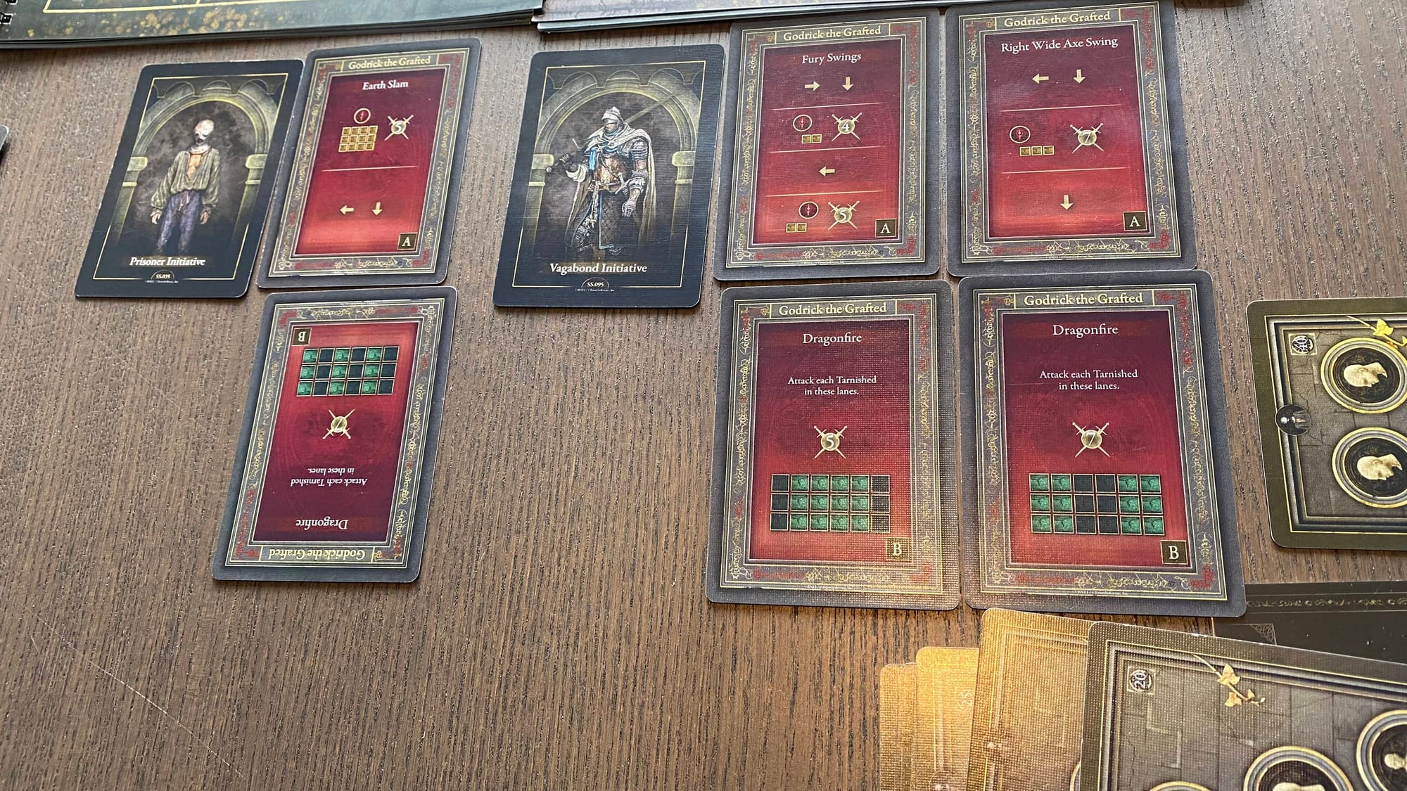 An example of the Marching Order against Godrick the Grafted. In his second stage, he gets additional cards dealt out representing his Dragonfire. Here, one of them is upside-down to represent being staggered which disables the card.