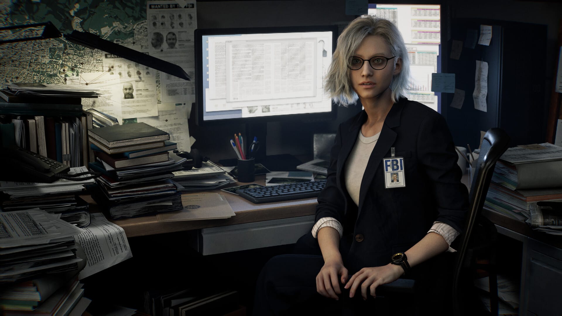 Grace sitting at her desk. She is a woman with light blonde hair. She has an FBI badge on. Her desk is a mess with files and books and her computer is on.