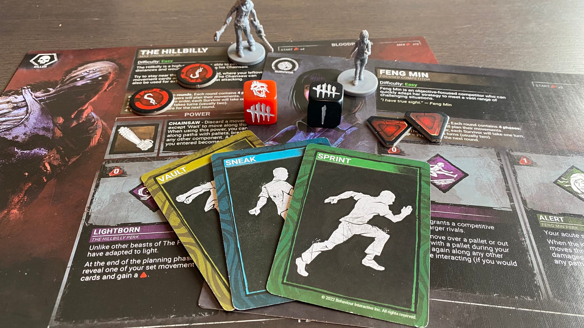 Various game components, including two character boards and their minis, as well as some cards, dice, and tokens