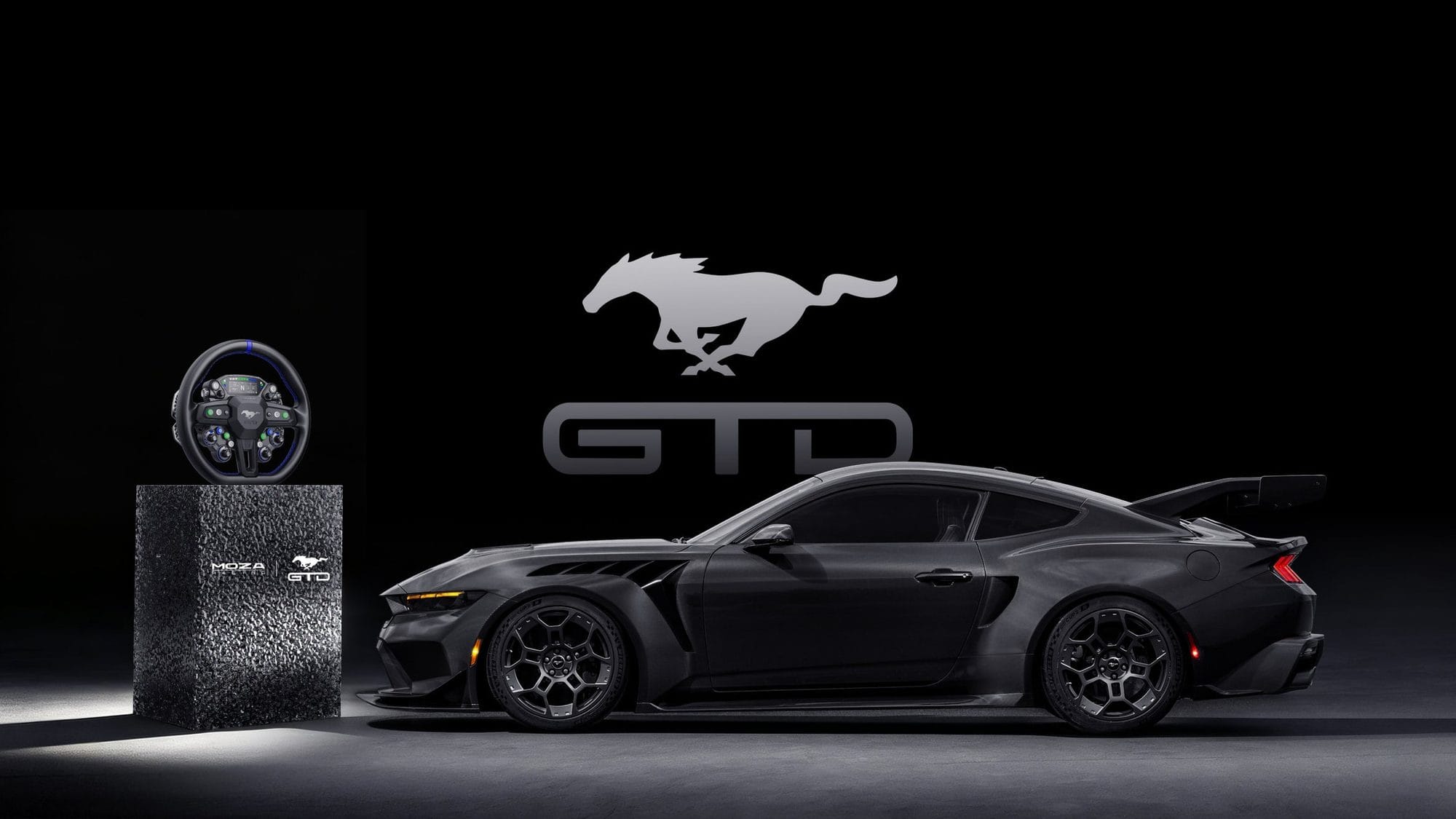 MOZA Ford Mustang GTD sim racing wheel on a plinth beside a black Ford Mustang GTD