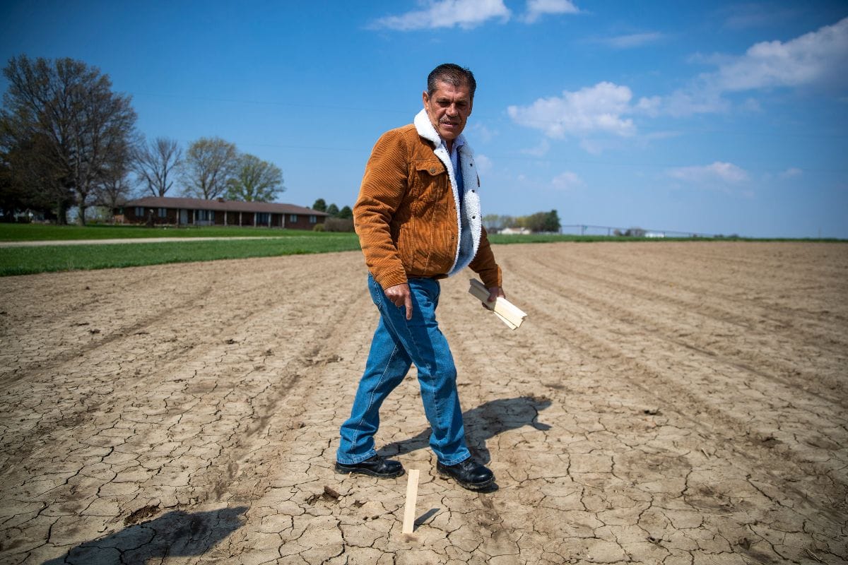 A farmer in a brown jacket and blue jeans walks dry fields ready for planting.