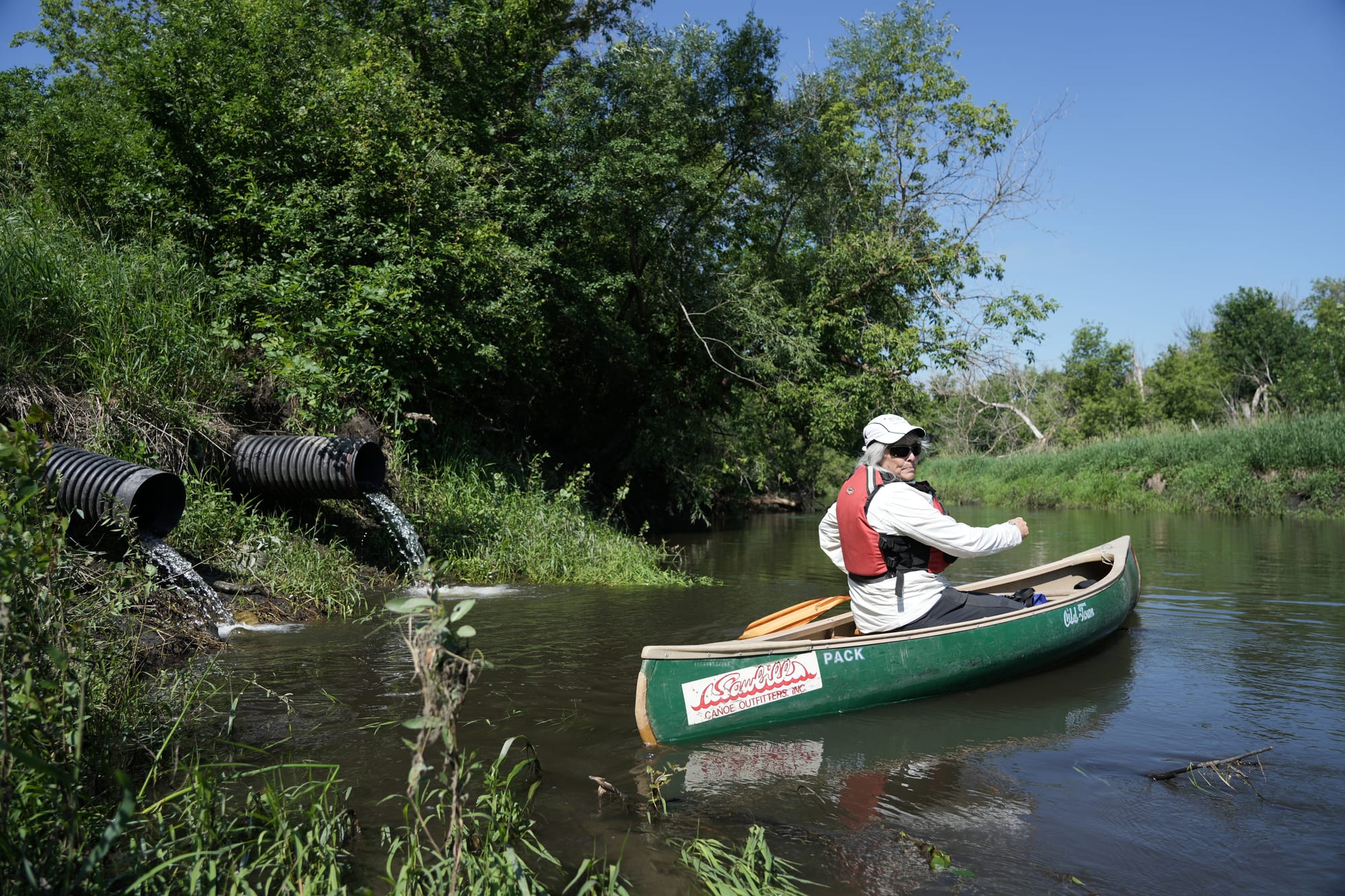 A person paddles in a canoe by a drain pipe
