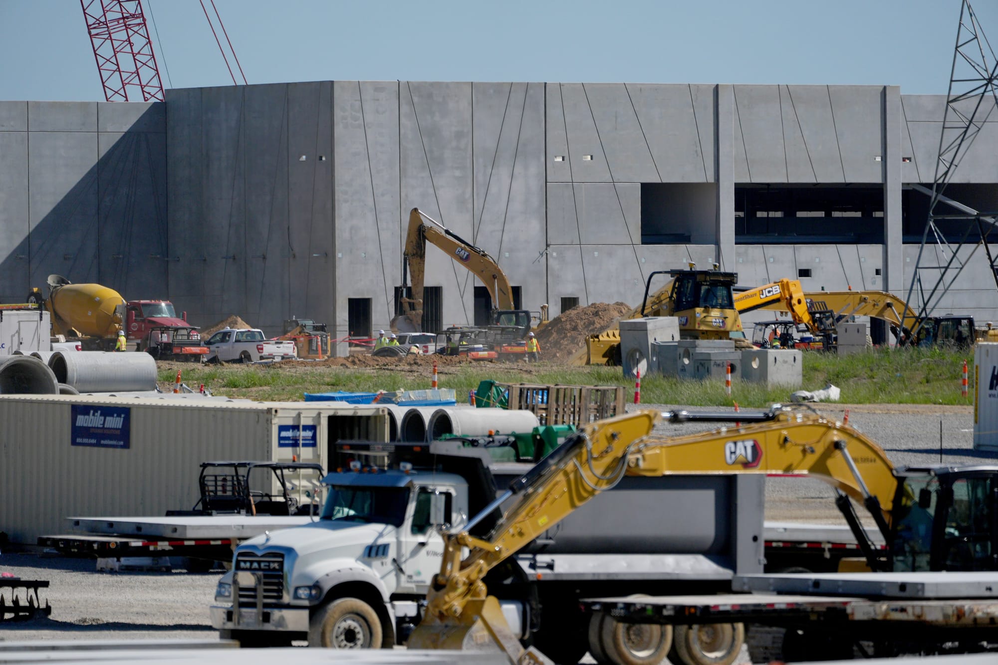 Bulldozers and heavy trucks operate at a busy construction site, where a concrete building looms in the background