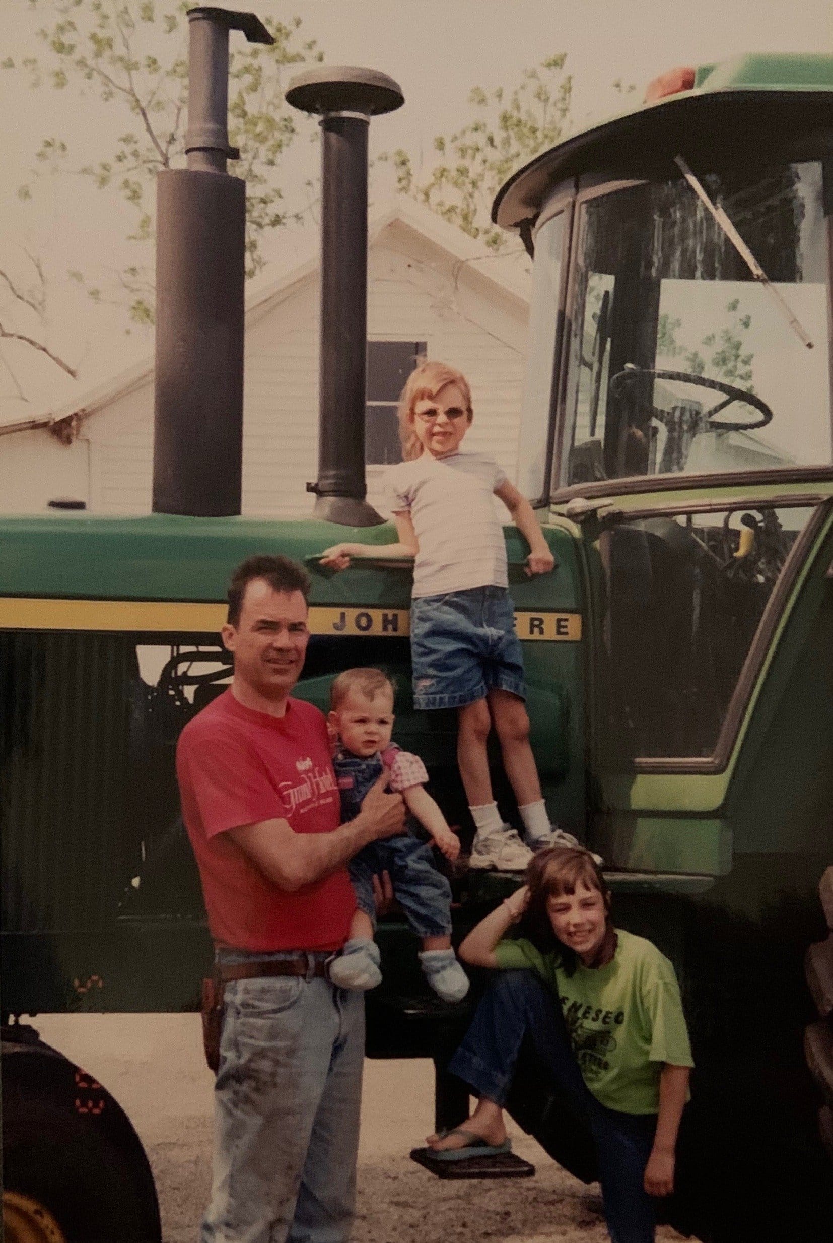 Father poses with his three daughters in front of a John Deere tractor