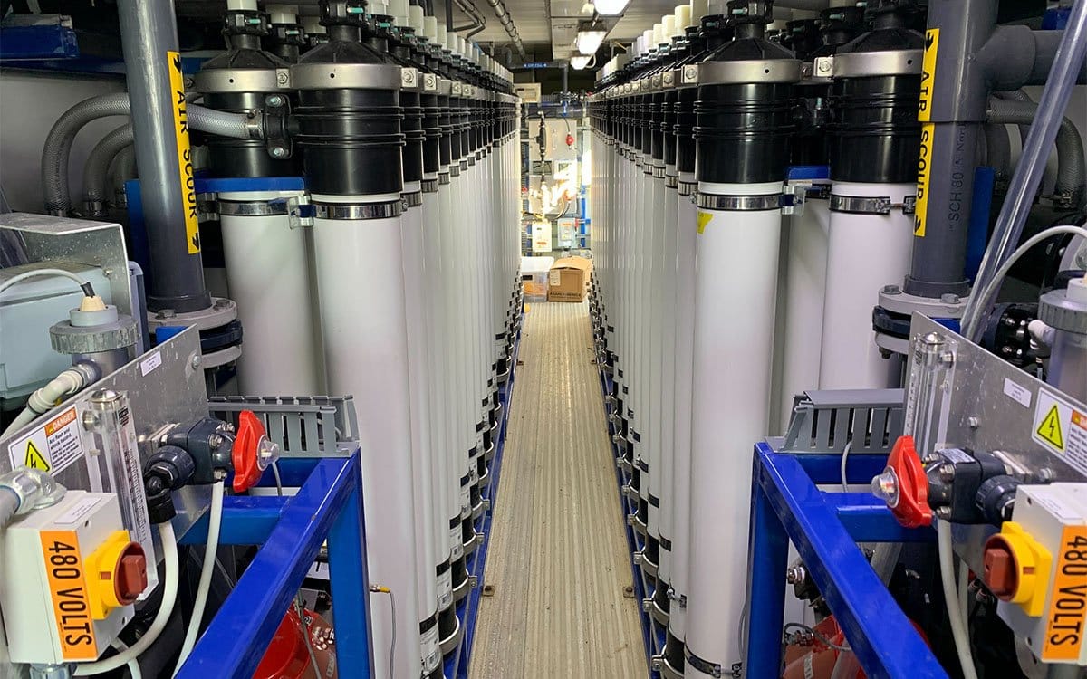A narrow hallway is formed between rows of white tubing in a room full of various technical equipment