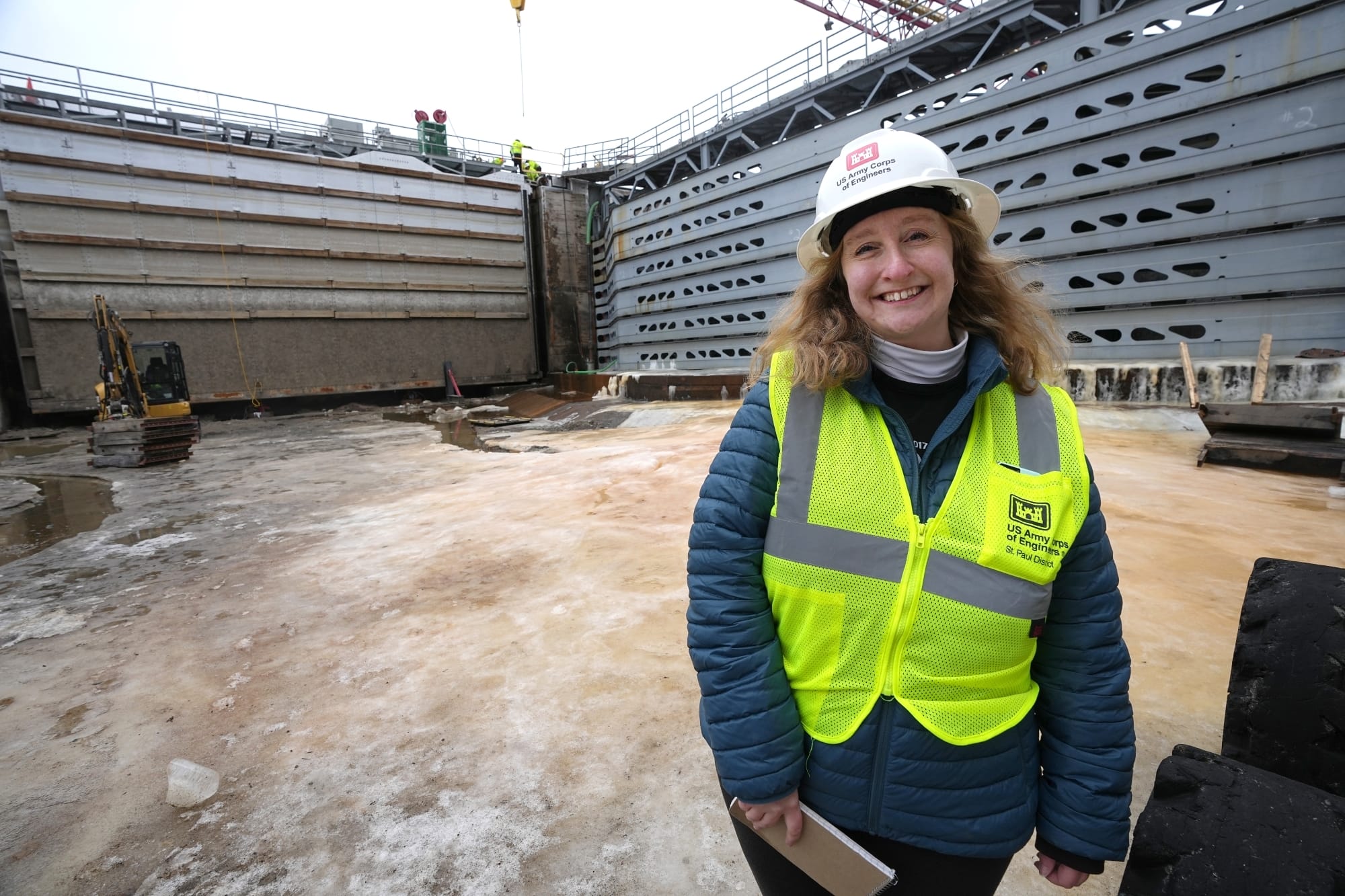a reporter in a hard hat and safety vest stands in an empty lock