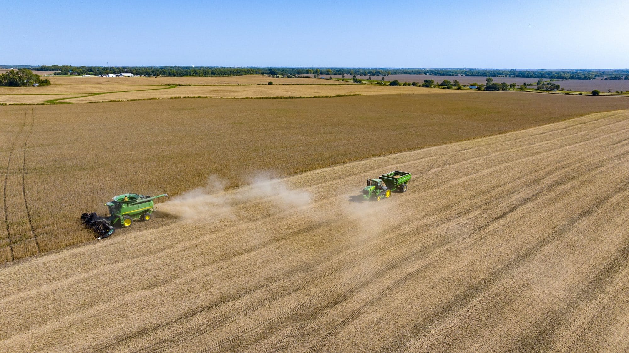 Two industrial farm vehicles move across a yellow field