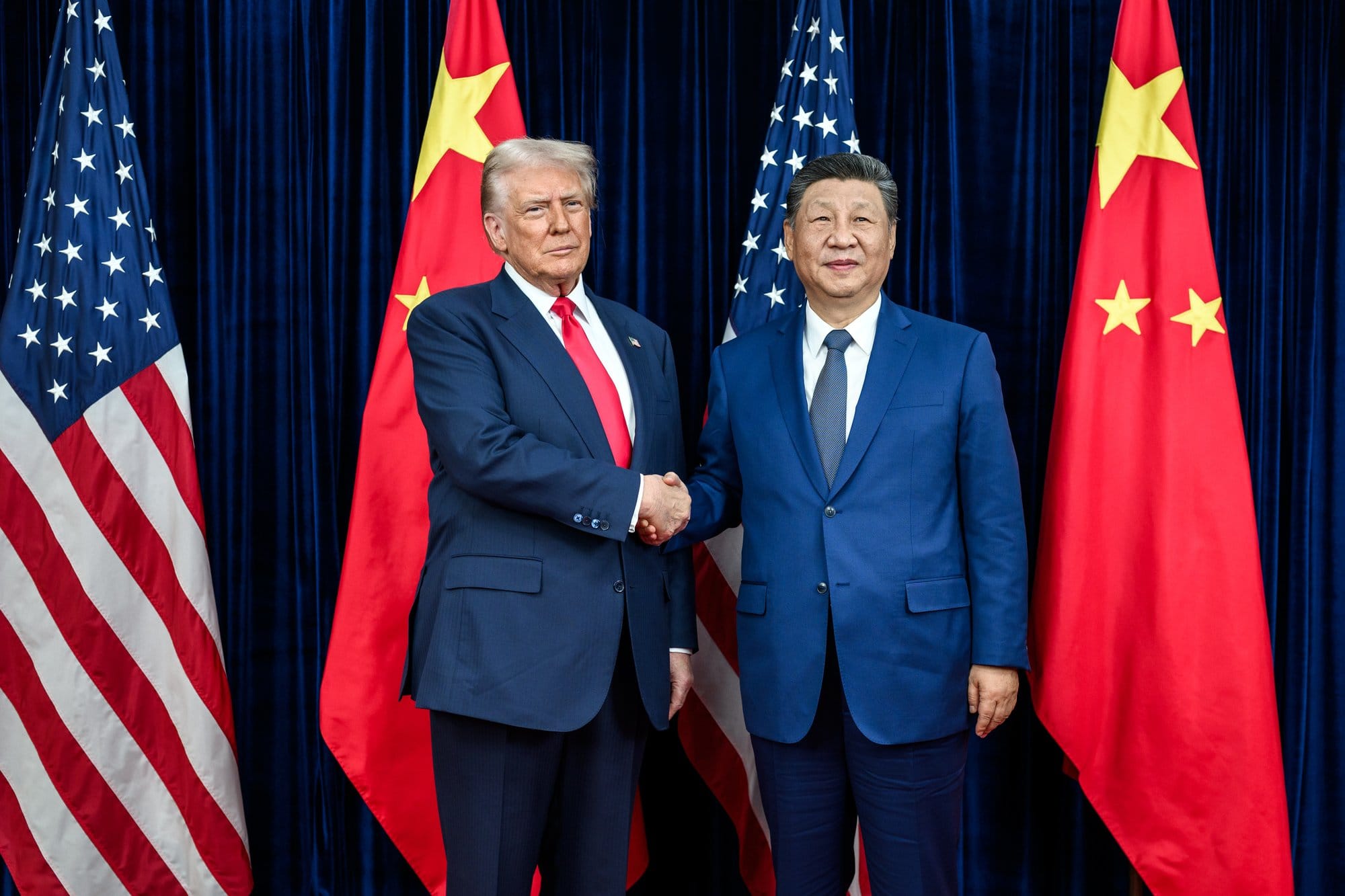 President Donald Trump shakes hands with Chinese President Xi Jinping on a stage with each country's flag behind them