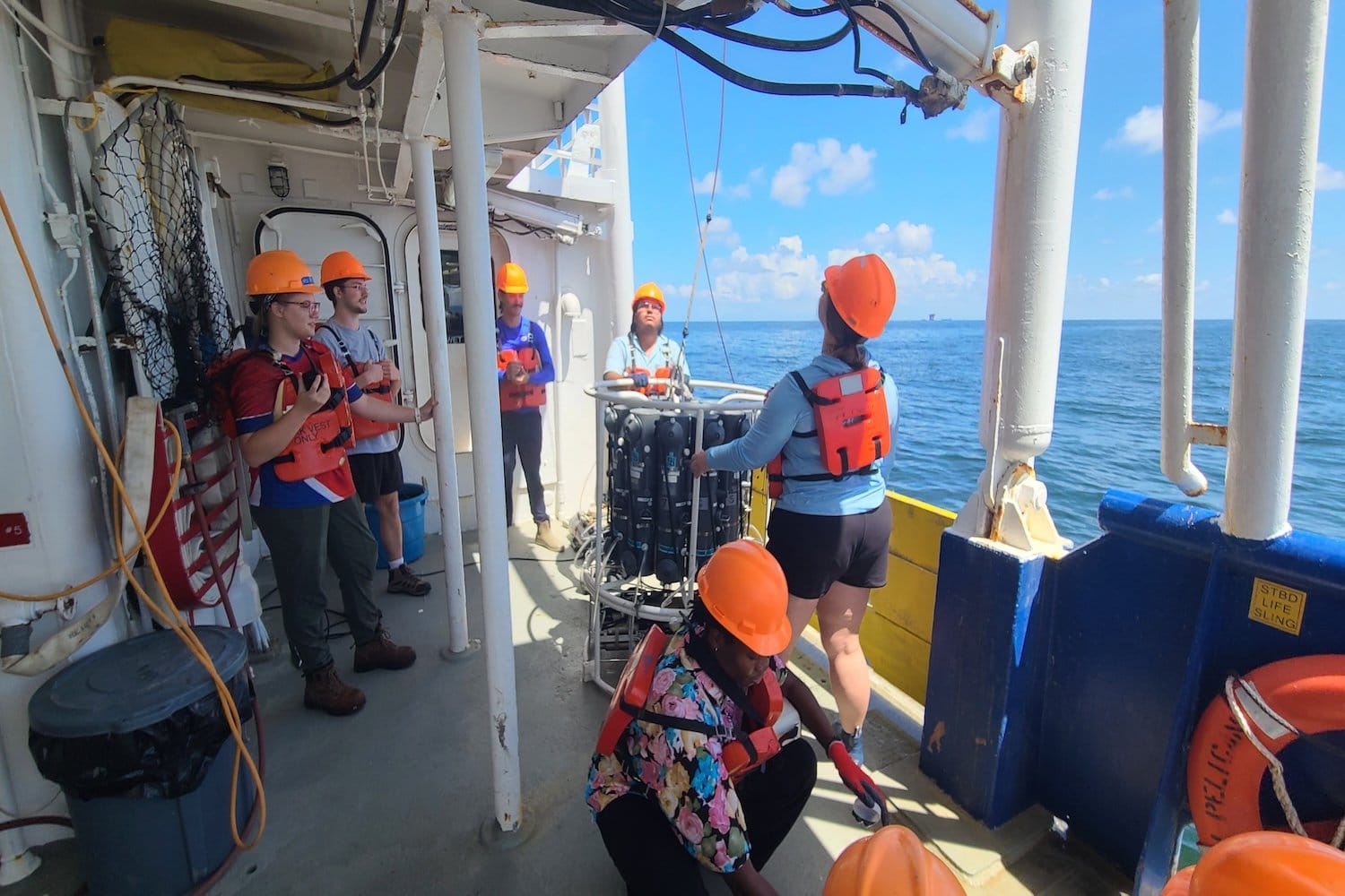 Students Jorddy Gonzalez and Lily Tubbs retrieve a CTD sensor package after measuring dissolved oxygen during the annual hypoxia cruise, while other students watch.