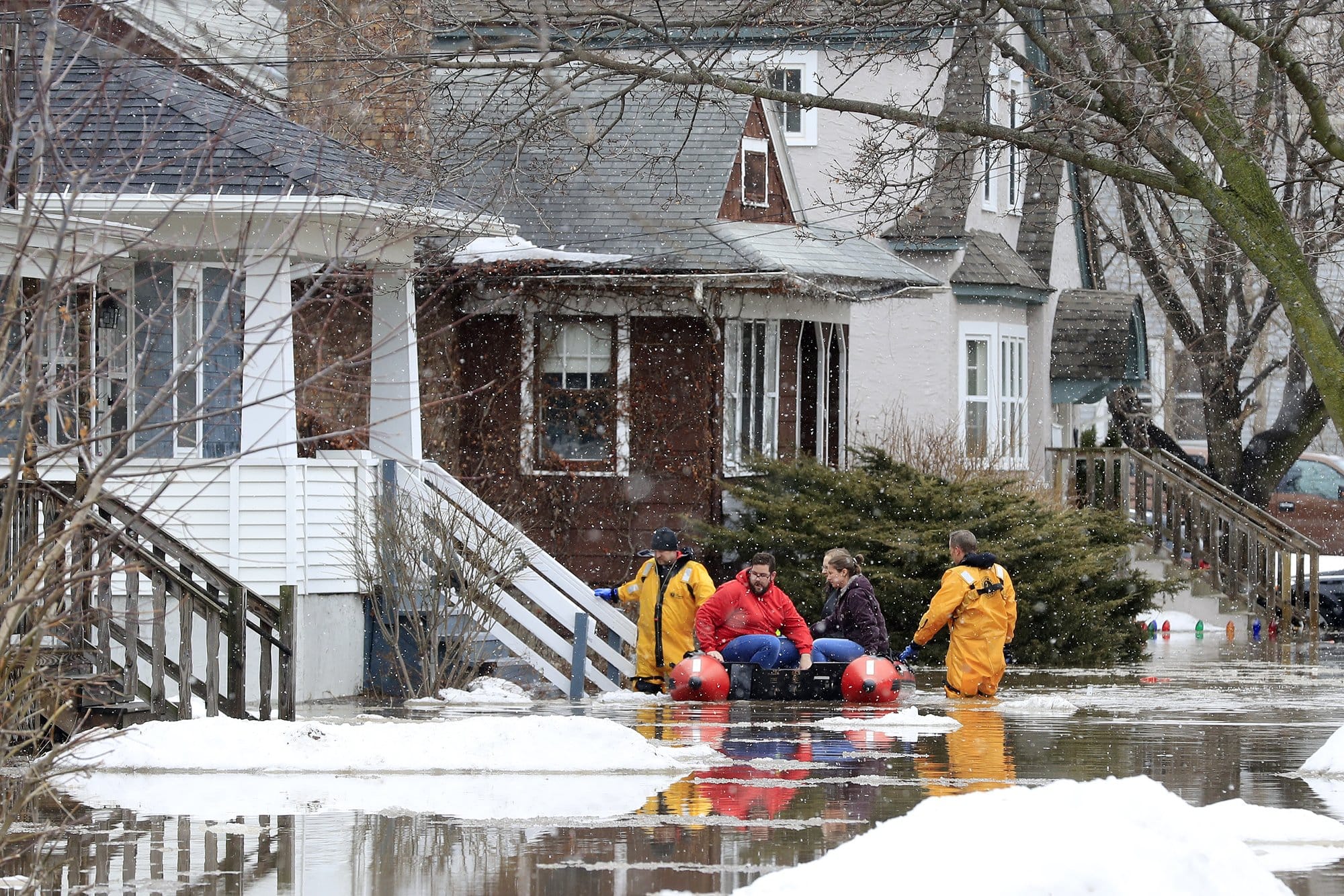 Firefighters assist residents in evacuating their homes due to East River floodwaters in Green Bay, Wisconsin. The streets are flooded with knee-level water.