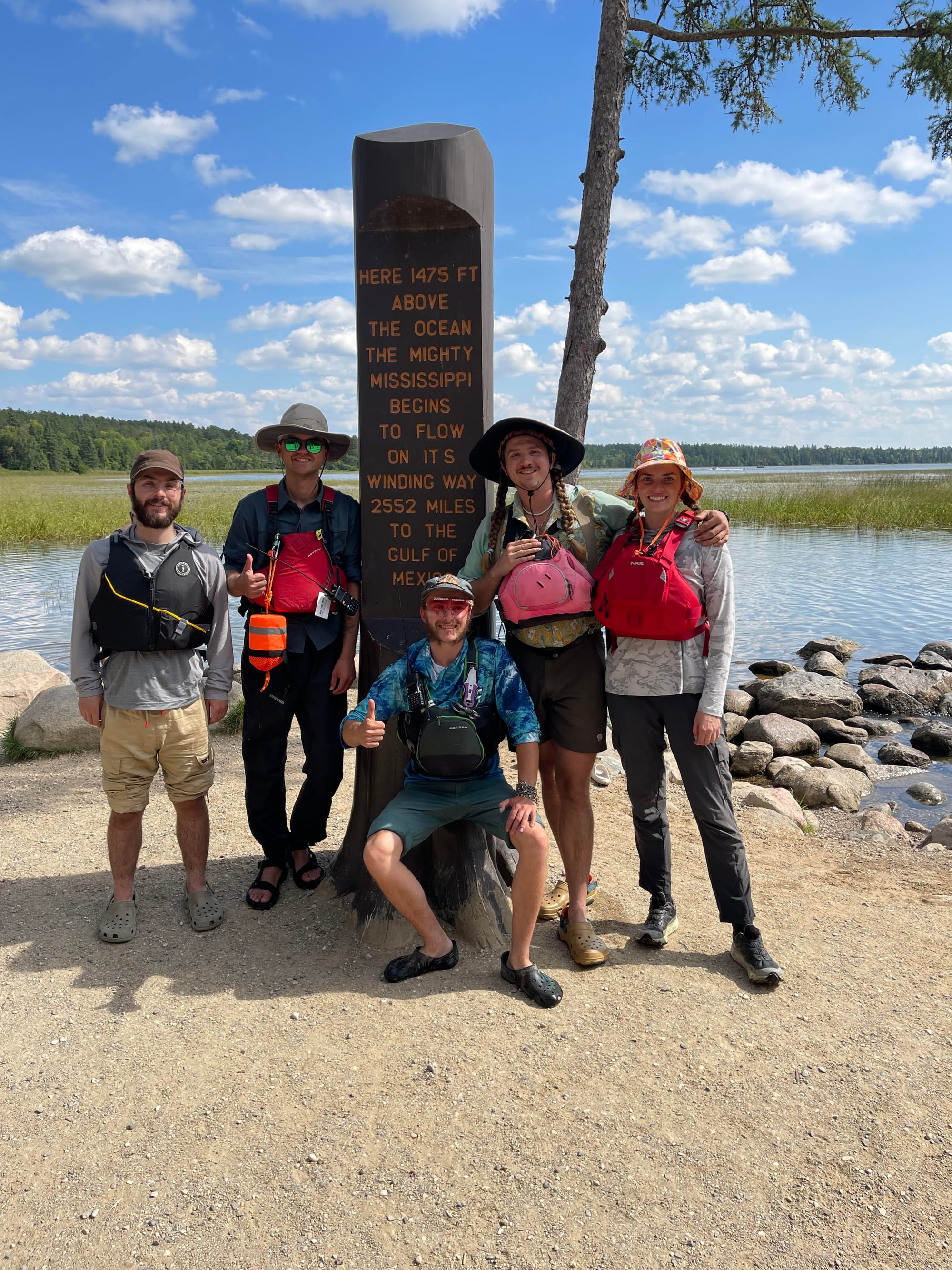 Five friends at the start of their paddling journey pose in front of the Headwaters Monument at Lake Itasca.