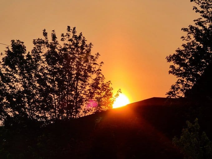 The sun rises over a roof. The sky is a vibrant orange