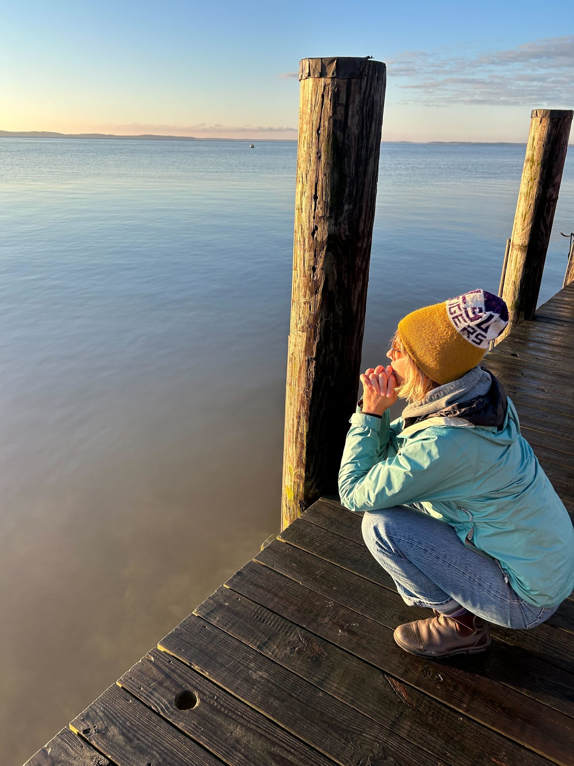 A reporter squats on a dock and watches the sunrise