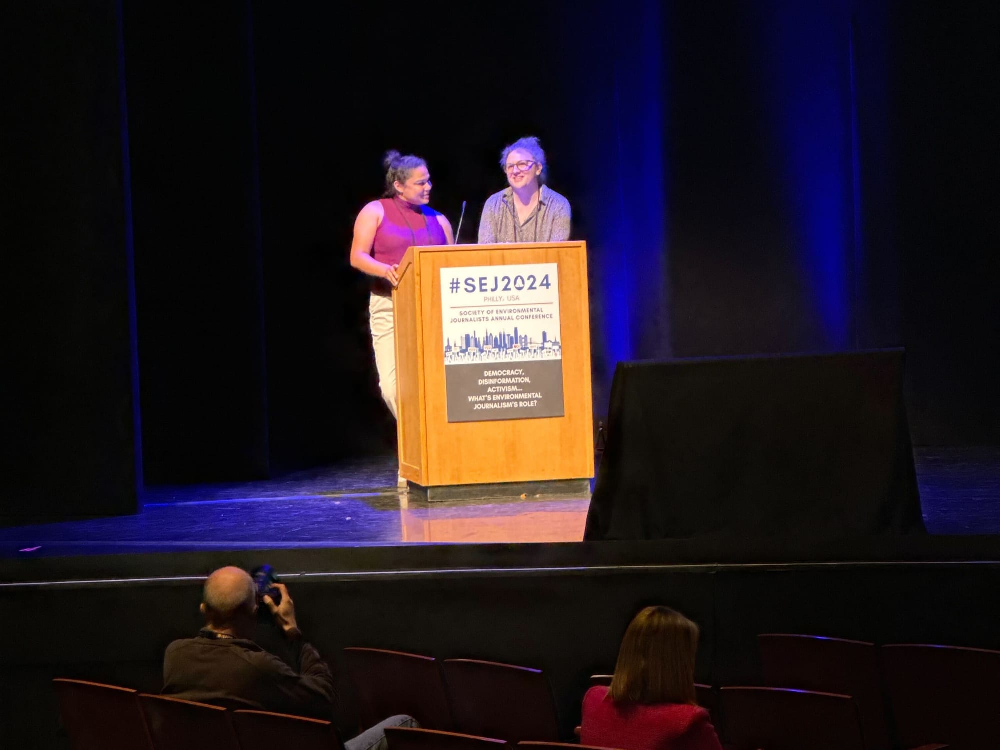 two women speak at a podium on a stage