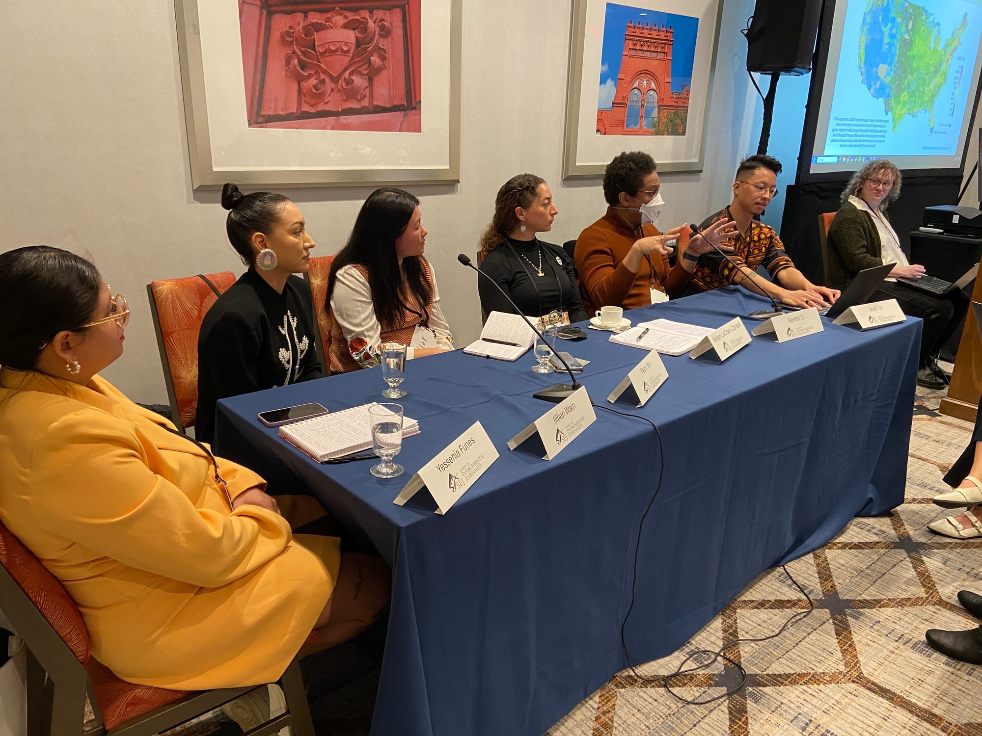 Panelists sit at a table and present to a room