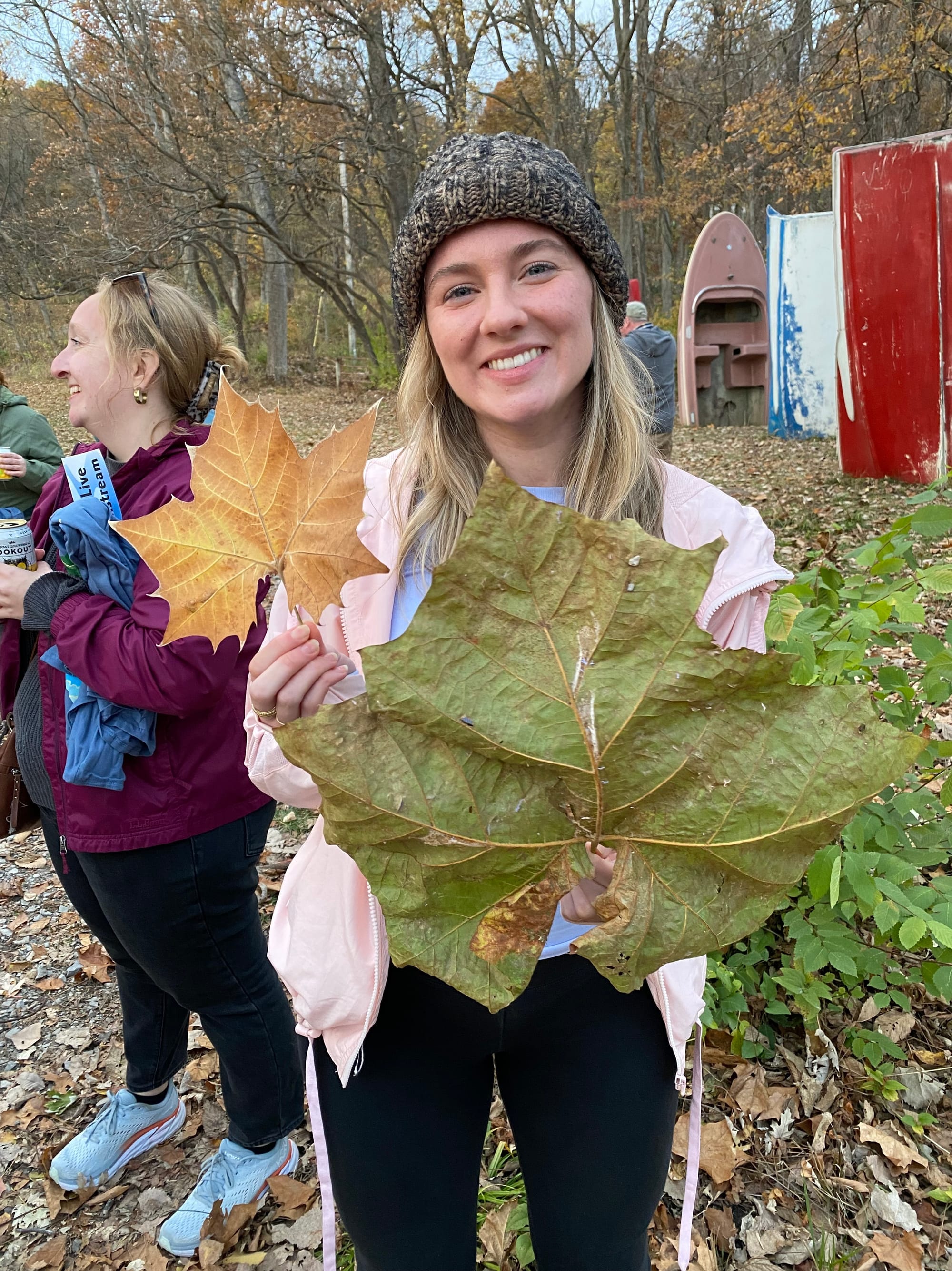 A woman holds two huge leaves and smiles 