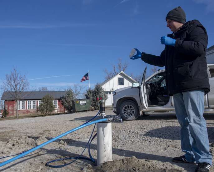 A scientist takes a water sample at a pump