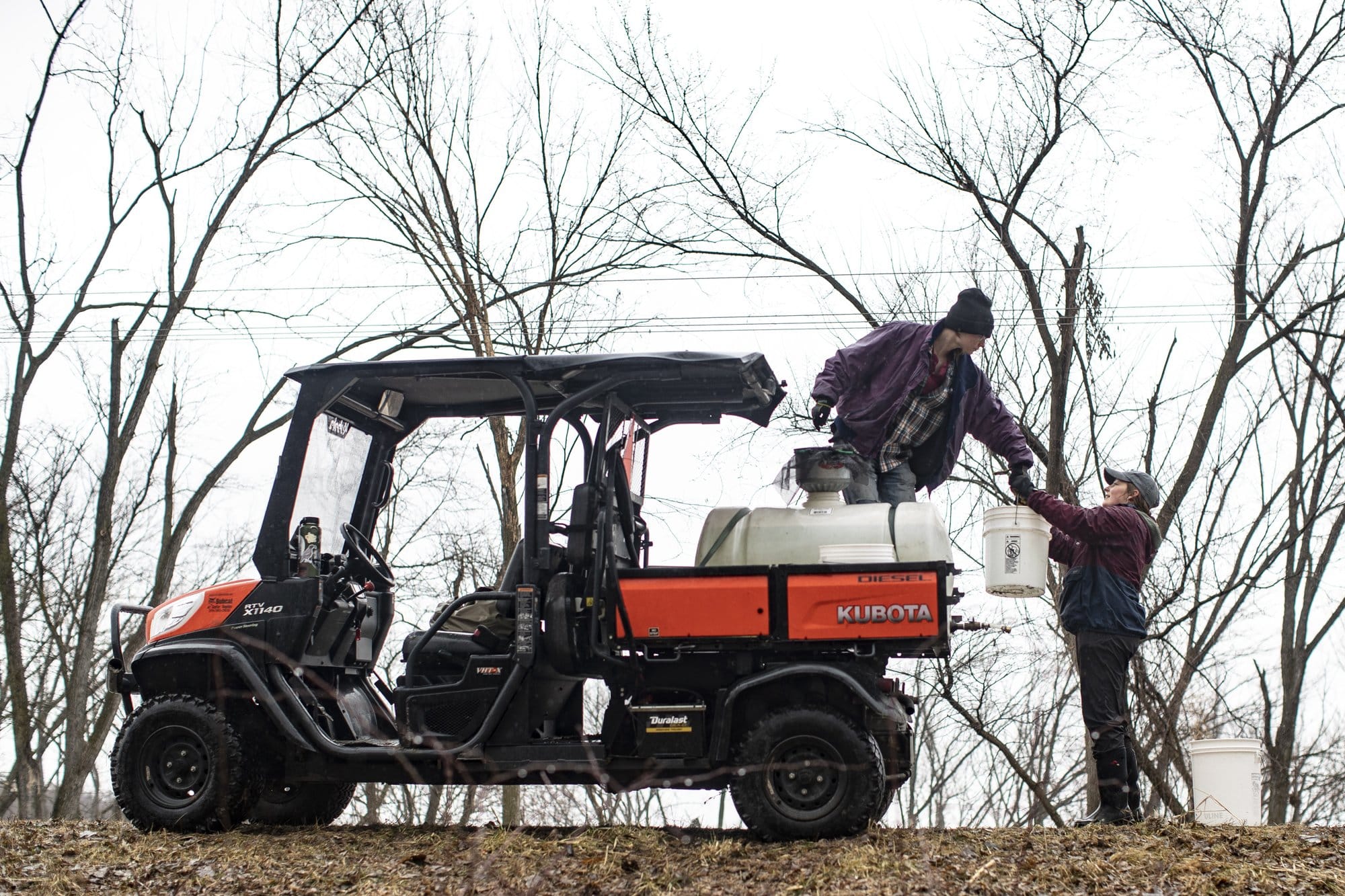 A worker in a farm gator hands off a bucket to another worker