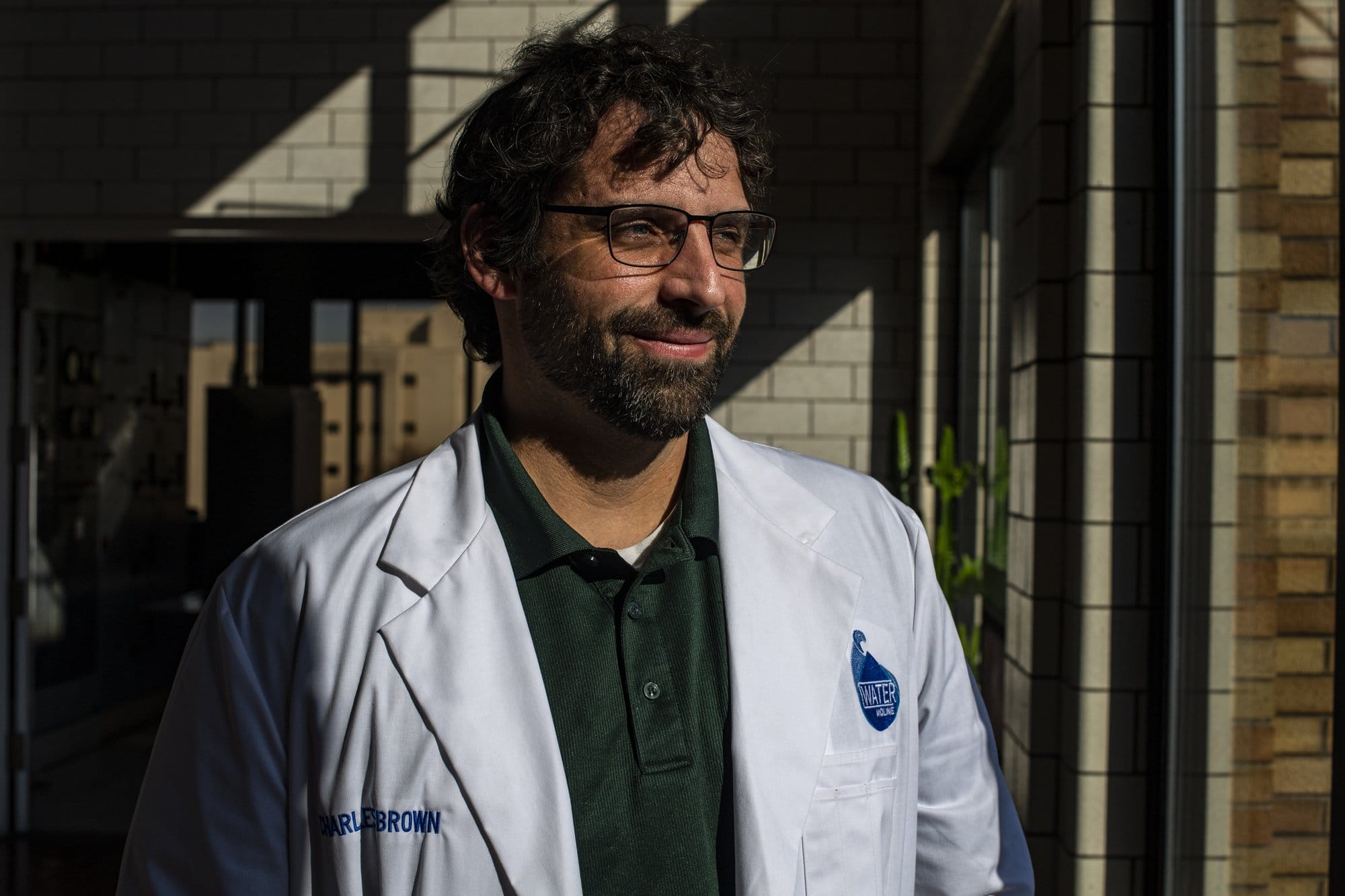 A man in a lab coat and glasses smiles as he looks out the window