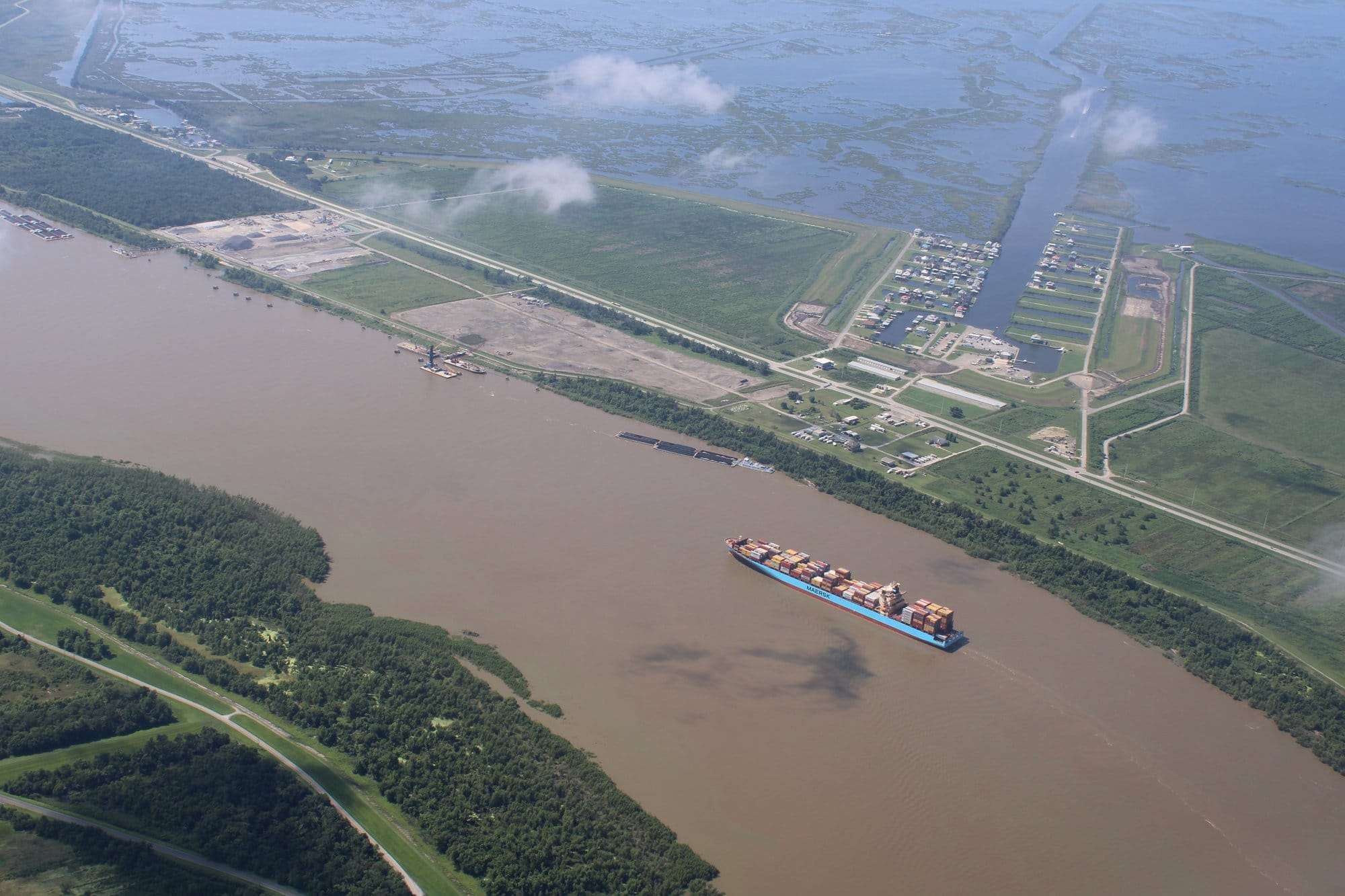 Aerial view of a ship traveling along the Mississippi River, surrounded by wetlands and industrial areas.