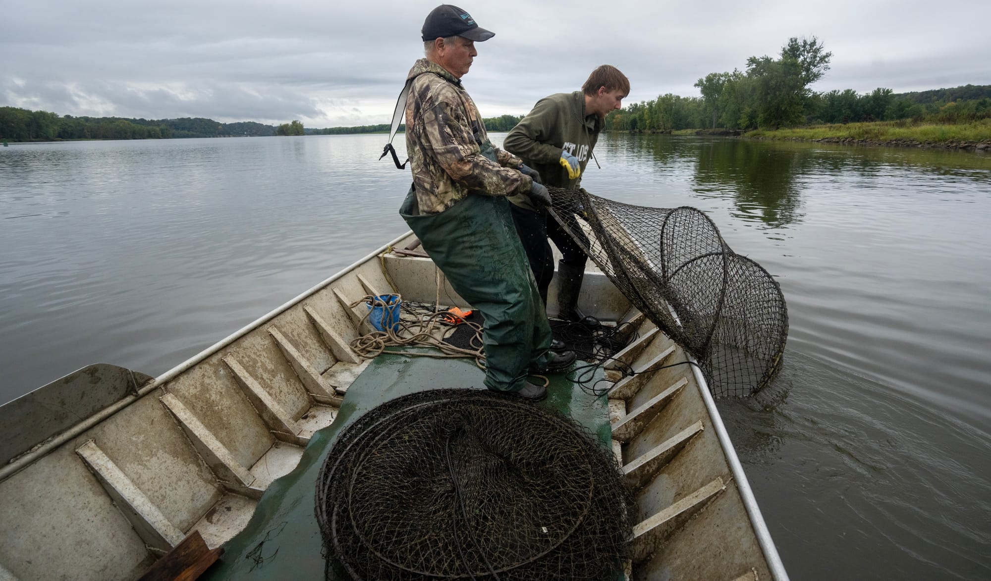 Two men lift a net into a fishing boat on the river