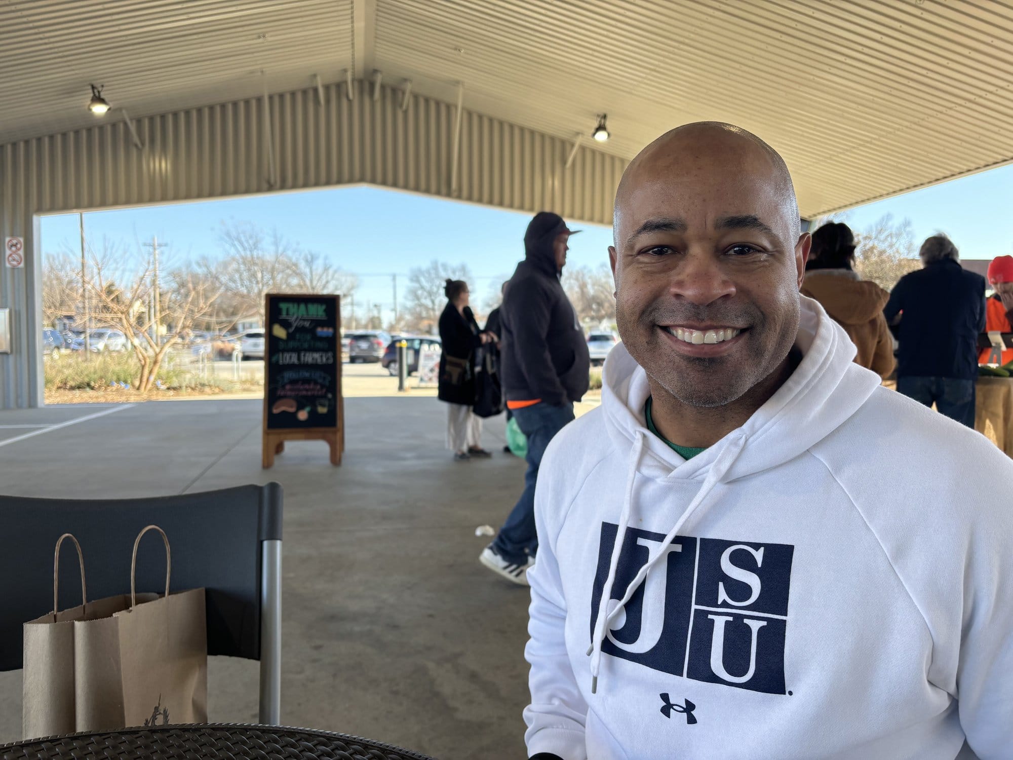 David Lovelady poses for a photo beside a chair holding his purchase of organic food from Happy Hollow Farm at the Columbia Farmers Market in Missouri.