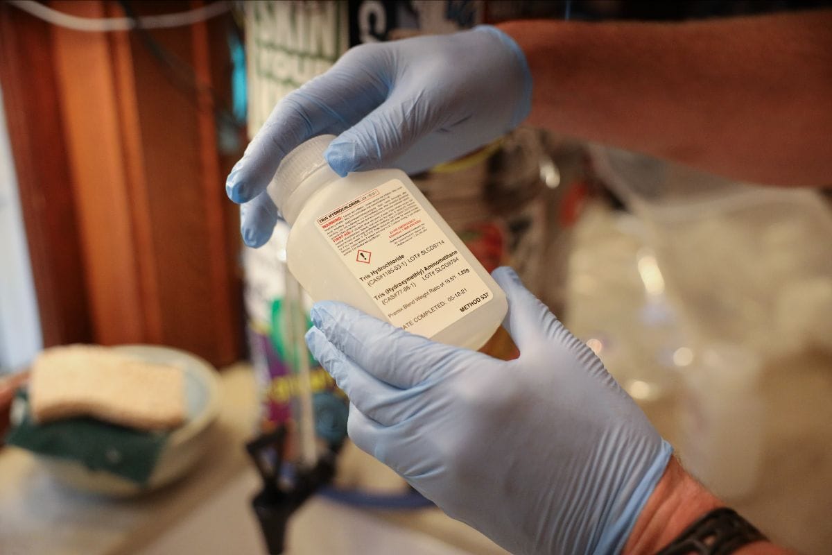Hands in rubber gloves hold up a bottle of chemicals