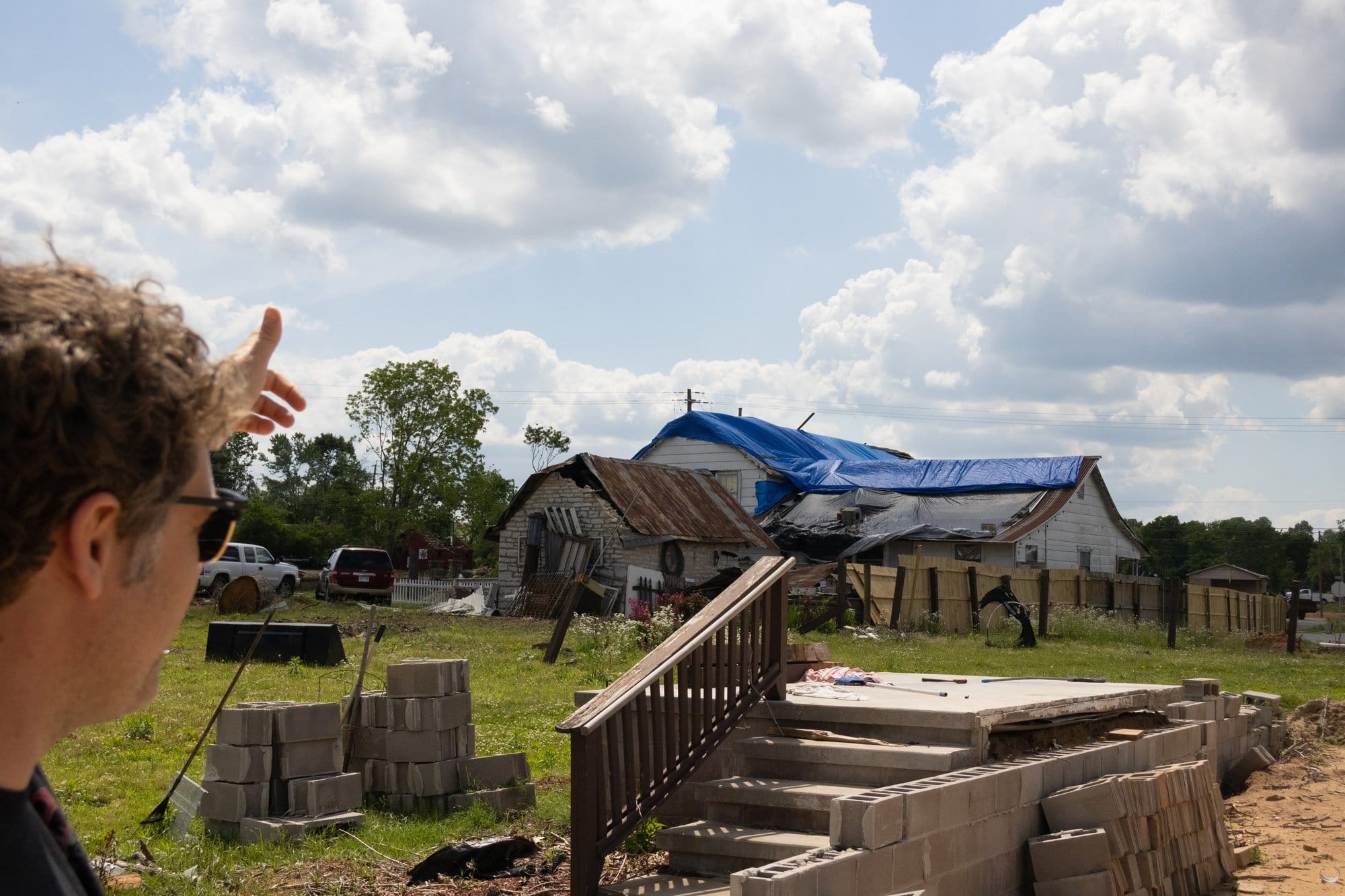 A man points to damaged buildings with stacks of cinder blocks around him