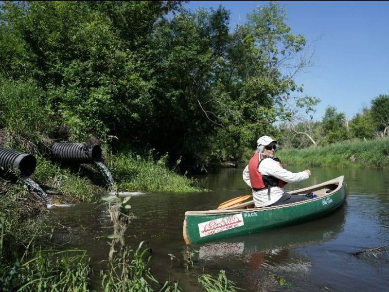 A figure paddles in a canoe past a discharge pump