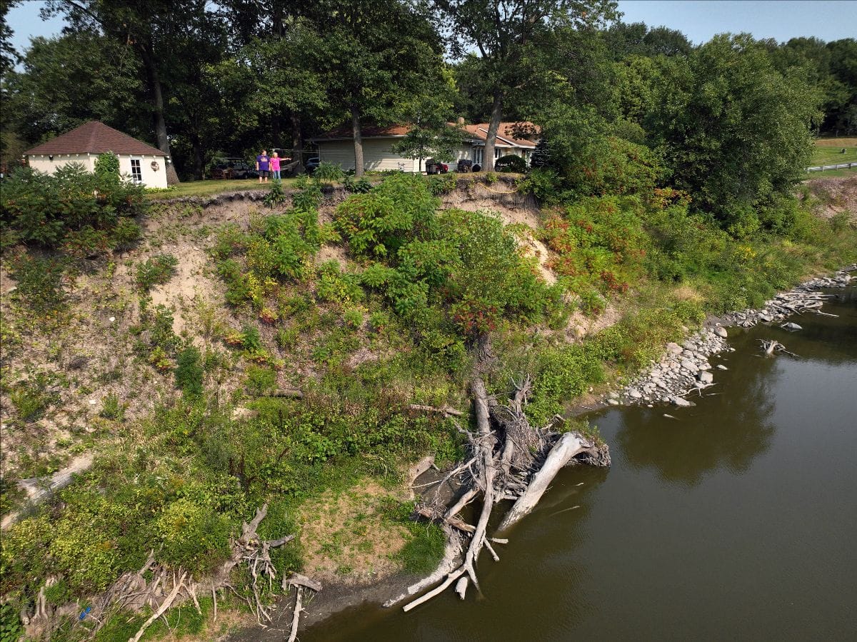 Two figures stand beside a steep river bank