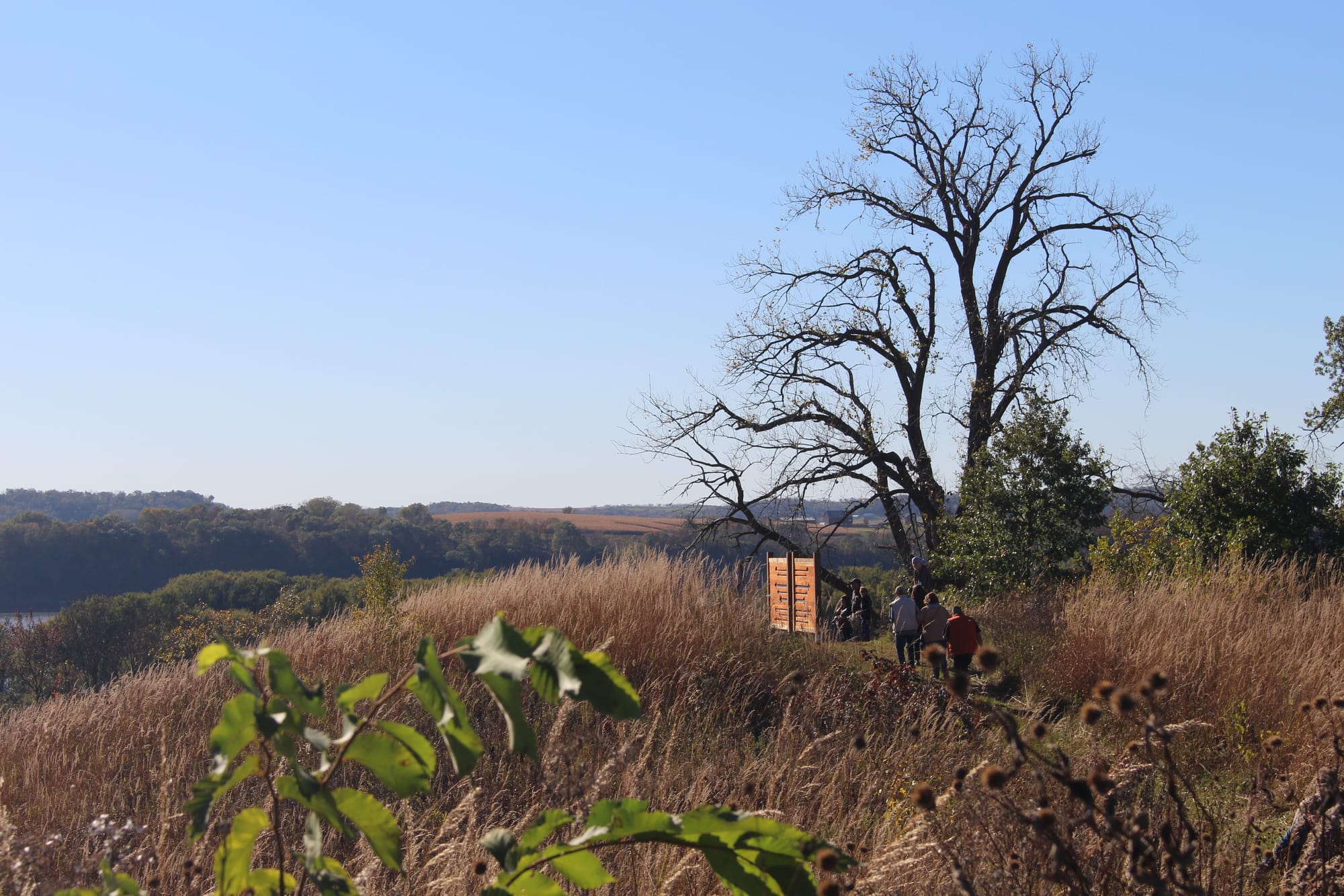A small group of people walks down a trail on a grassy bluff above the river