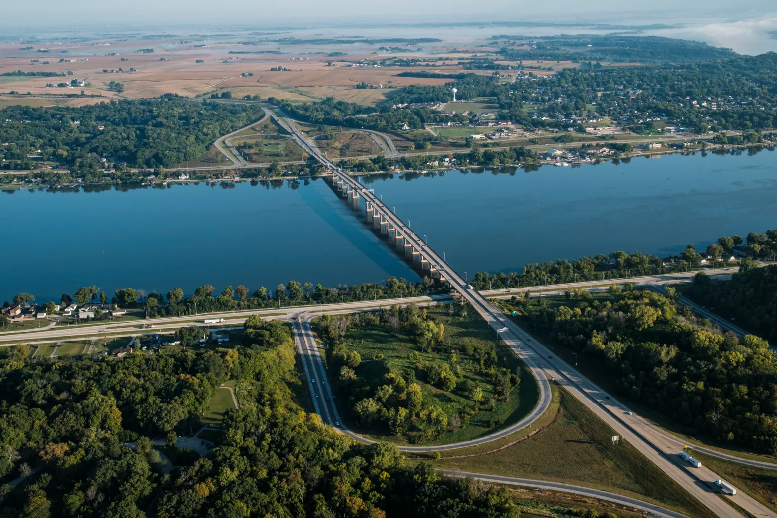 Aerial view of Interstate 80 crossing the Mississippi River, surrounded by highways, trees, farmland and communities along both sides of the river.