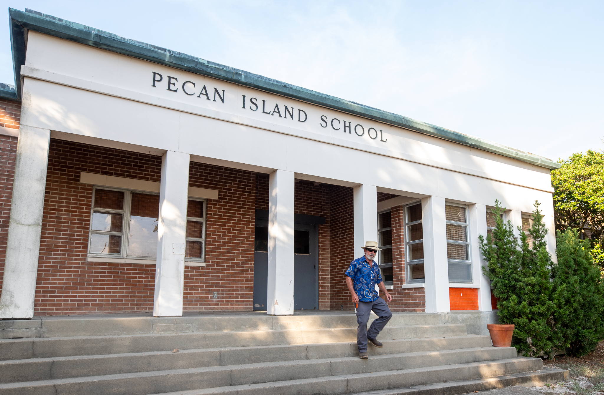 A man in a wide brim hat walks down the steps of Pecan Island School
