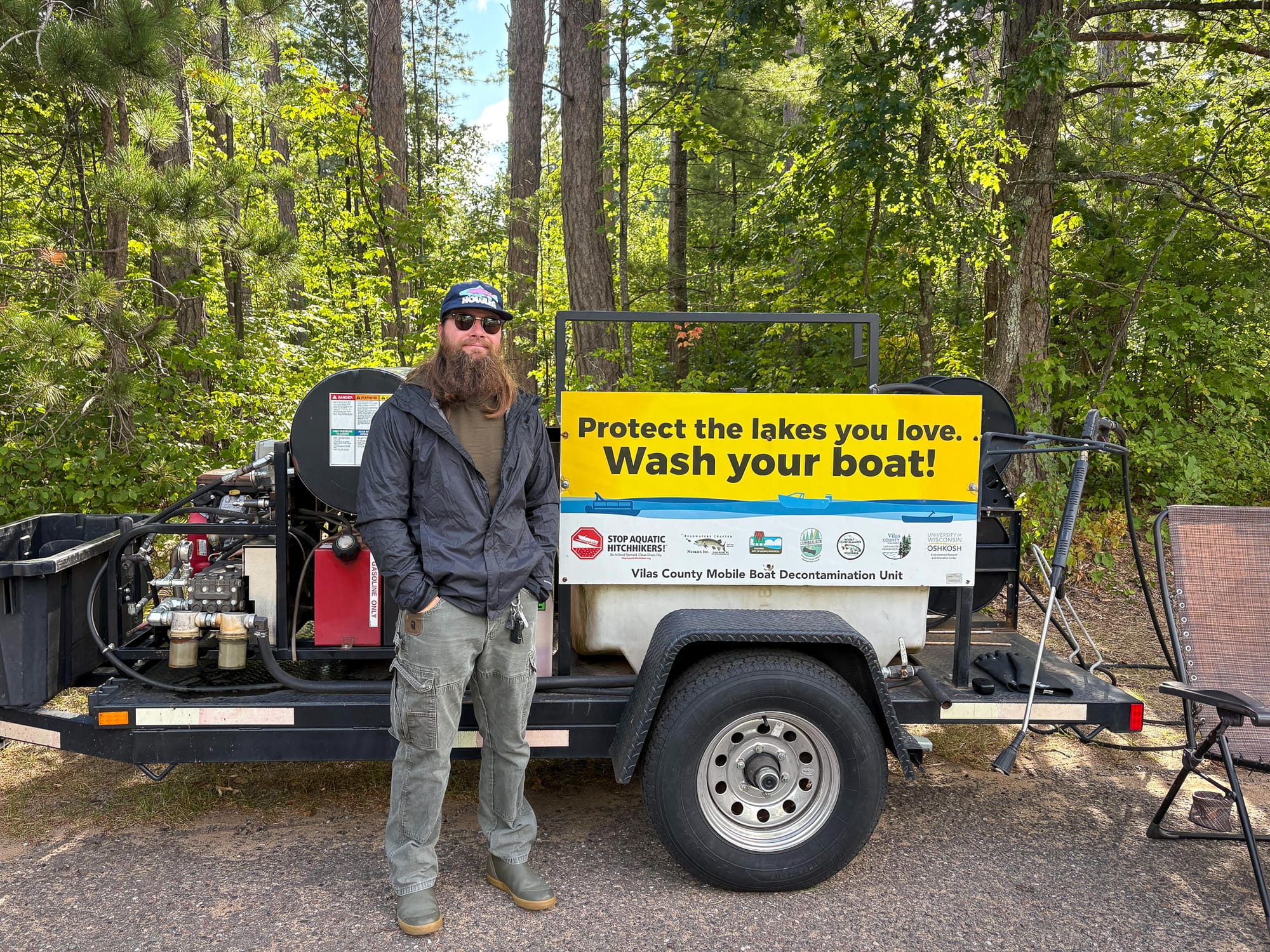 A man in water-resistant clothing stands in front of a trailer containing decontamination equipment.
