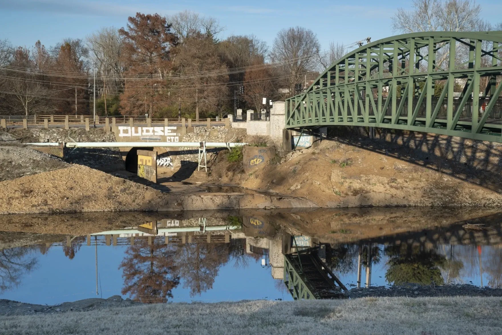 A green metal bridge crosses the River Des Peres in south St. Louis, where a thin layer of water covers the channel beneath it.