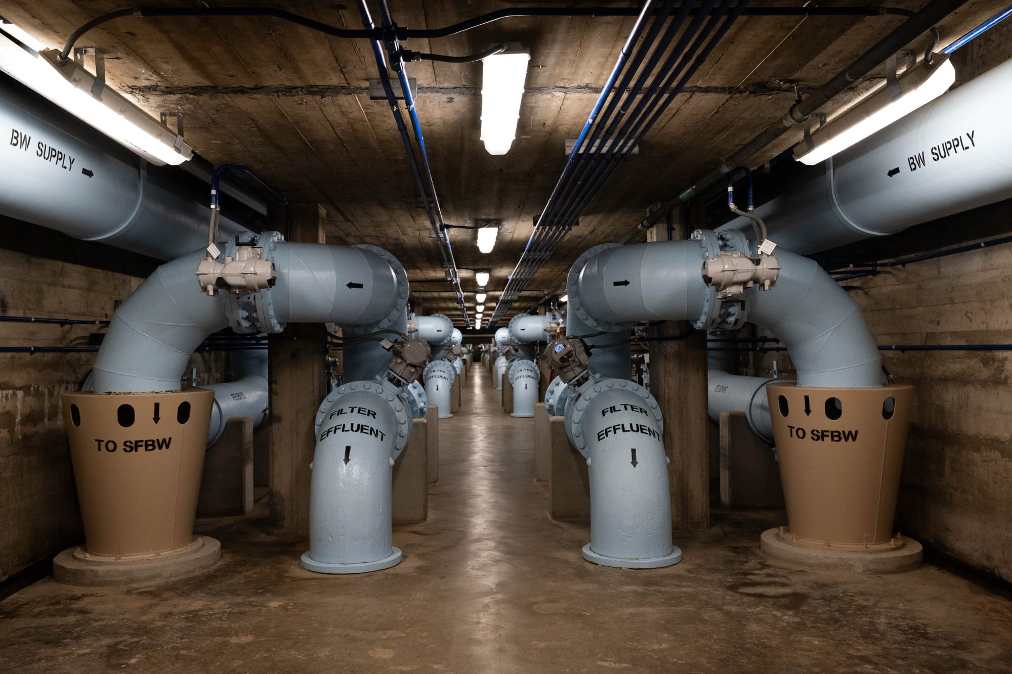 Large gray and brown pipes run through a long corridor.