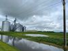 A flooded farm field below a grain silo under a grey sky.