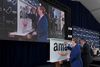 A white man in a blue suit signs a steel, Amazon-branded beam with a sharpie at a press conference